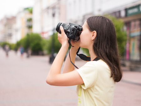 Cheerful young casual woman tourist make shots on dslr camera outdoors on city street. Vacation...