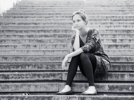 Sad lonely young woman sitting on steps. Portrait of serious girl with facial expression outdoors. Black and white imageの写真素材