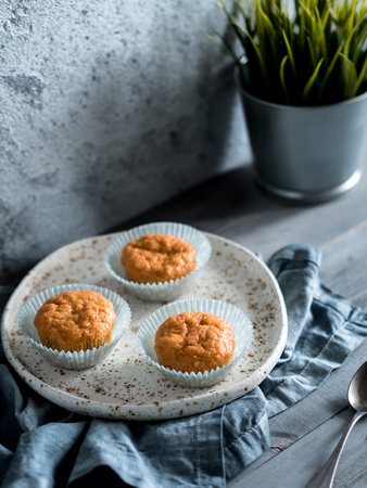 Homemade muffins on craft plate over gray wooden table. Carrot cupcakes with copy space. Toned image in scandinavian style. Copy space. Toned image in scandinavian style.の写真素材