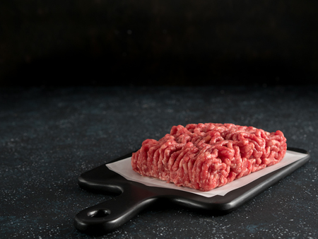 Fresh raw minced beef on backing paper and cutting board over black cement background with copy...