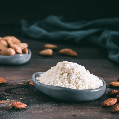Almond powder in gray trendy plate and almonds on dark wooden table. Almond flour and peeled kernel almonds. Copy space.の写真素材