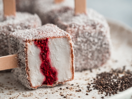 Homemade raw lamington ice cream pops on light background. Australian sweet dessert lamington with chia and raspberries jam, chocolate and cocoa coat. Vegan food recipe and idea. Copy space. Close upの写真素材