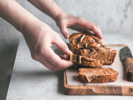 Butter-free,sugar-free banana bread with oat flour,soft curd cheese,honey. Woman hand with slice of banana bread on gray table. Ideas recipe healthy diet breakfast. Selective focusの写真素材