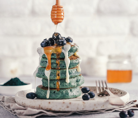 Blue pancakes with spirulina, dressed blueberries, white vanilla sauce and honey. Ideas and recipes for healthy breakfast with superfood ingredients.の写真素材