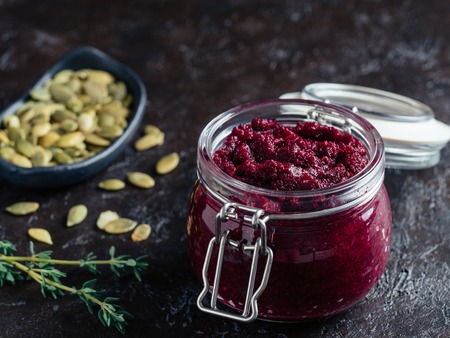 Beetroot pesto or hummus. Homemade beet pesto sauce in glass jar,pumpkin seeds and fresh thyme on dark black background. Copy space for text. Ideas and recipes for healthy vegetarian detox diet foodの写真素材