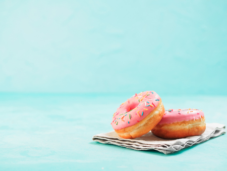 Two pink donuts on blue concrete background with copy space. Colorful donuts with copyspace. Glazed doughnuts with sprinklesの写真素材