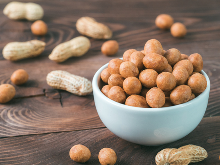 Peanut snack for beer, wine, party bar. Salted peanuts in coconut glaze on brown wooden table. Copy...