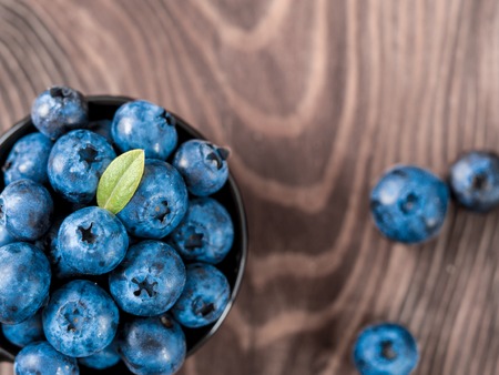 Blueberries in small black bowl on brown wooden tabletop. Top view of blueberry with copy space for text. Flat lay.の写真素材