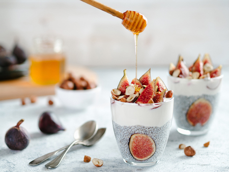 Healthy chia pudding with yogurt, figs and nuts in glass. Ideas and recipes for healthy breakfast, snack or dessert. Honey drips into glass with chia seeds pudding. Copy space for text.の写真素材