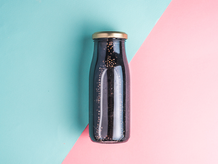 Detox activated charcoal black chia water or mocktail on colorful blue and pink background. Bottle with black chia infused water.Detox drink idea and recipe.Vegan food and drink.Top viewの写真素材