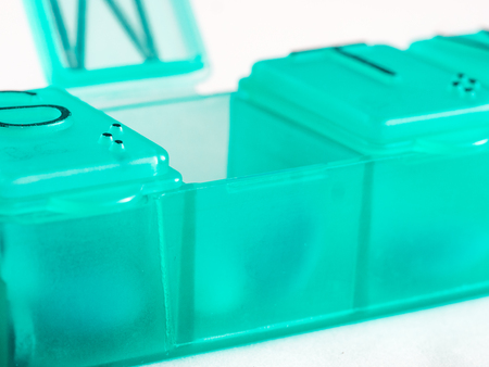 Extreme close up of seven day pill box with pills. Green pill-box with tuesday pills visible. Open pill box on white backgroundの写真素材