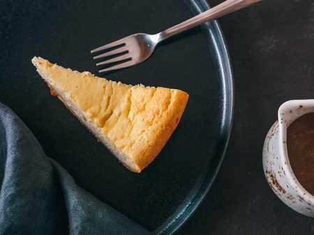 Plate with piece of cheesecake on dark background. Classic cheesecake, caramel sauce and dessert forks. Top view or flat lay.の写真素材