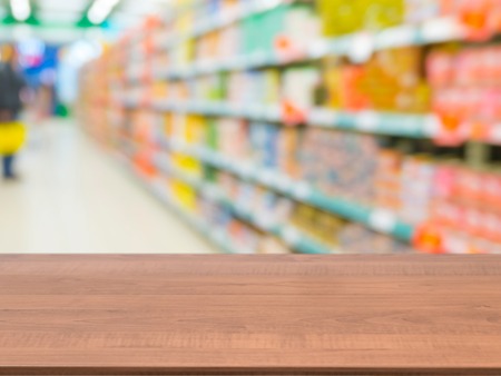 Blurred colorful supermarket products on shelves and perspective table for mockupの写真素材
