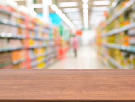 Blurred colorful supermarket products on shelves and perspective table for mockupの写真素材