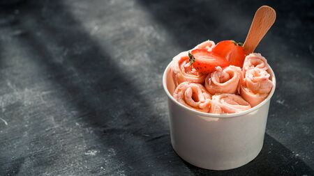 Rolled ice cream with strawberry in cone cup on dark rustic background. Strawberry iced rolls banner. Thai style rolled ice cream with copy space for text or design. Banner. Natural hard daylightの写真素材