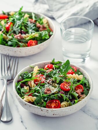 Warm salad with tuna, arugula, tomatoes, red bean, pasta. Idea and recipe for healthy lunch or dinner. Two bowls with warm salads on marble tabletop. Ideas and recipes for healthy dinner or lunchの写真素材