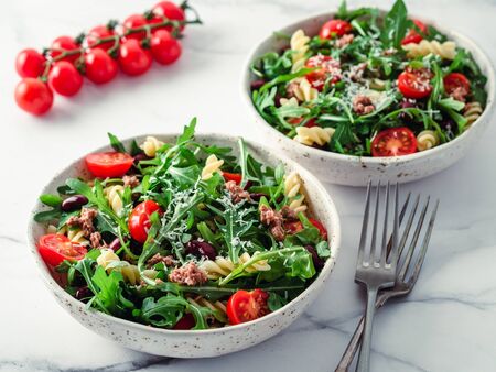 Warm salad with tuna, arugula, tomatoes, red bean, pasta. Idea and recipe for healthy lunch or dinner. Two bowls with warm salads on marble tabletop. Ideas and recipes for healthy dinner or lunchの写真素材