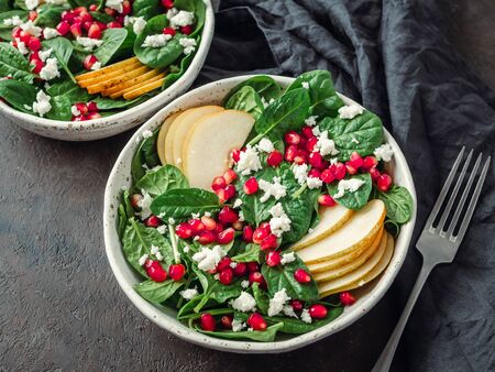 Vegan salad bowl with arugula, pear, pomegranate, cheese on black background. Vegan breakfast, vegetarian food, diet concept. Top view or flat lay. Copy space for text.の写真素材