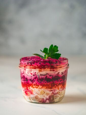 Layered salad herring under a fur coat on festive table, with fir tree and light garland. Traditional russian salad with herring and vegetables in glass jar. Copy space for text. Vertical.の写真素材