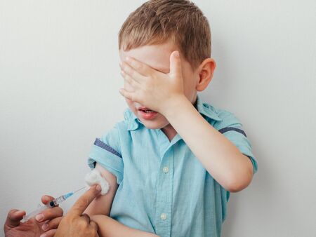 Little boy is afraid to vaccinate. Little caucasian baby boy in blue shirt covered his eyes with...