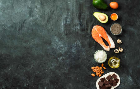Healthy fats sources concept. Different food ingredients rich good healthy fats on dark background. Copy space left. Top view or flat lay.の写真素材