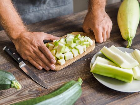 Zucchini harvest. Man slices zucchini cubes for freezing on wooden table. Farm organic zucchini harvestingの写真素材