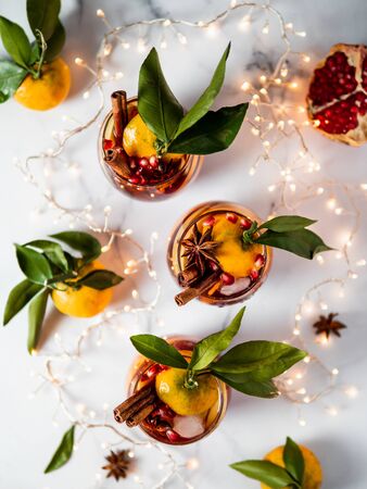 Winter sangria on white marble background. Holiday sangria in glasses with fruit slice, pomegranate and spices on decoration lighting chain tabletop. Top view or flat lay. Vertical.の写真素材