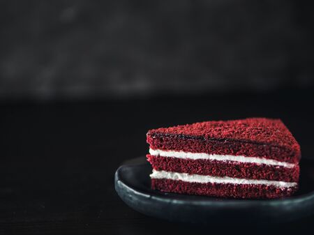 Piece of red velvet cake with perfect texture in matte plate on black tabletop. Slice of delicious homemade red velvet cake with raspberry and chocolate. Copy space for text.の写真素材