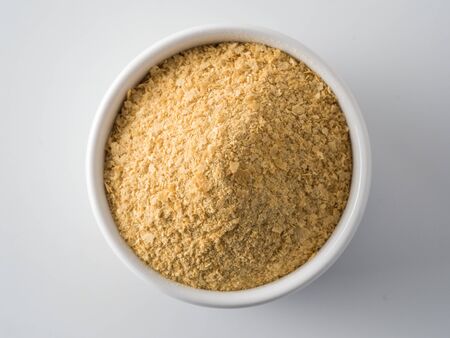 Nutritional yeast background. Nutritional inactive yeast in small white ctramic bowl. Copy space. Top view. Nutritional yeast is vegetarian superfood with cheese flavor, for healthy dietの写真素材