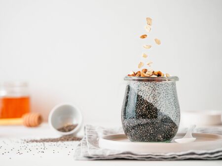 Healthy breakfast concept and idea - two colors chia pudding with organic raw almond. Glass jar with black charcoal and white vegan milk chia pudding with falling chopped almond. Copy spaceの写真素材