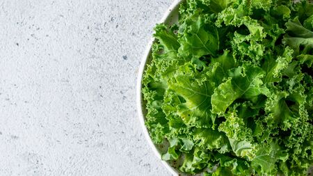 Kale close up. Green vegetable leaves, top view in white craft bowl over gray cement background....