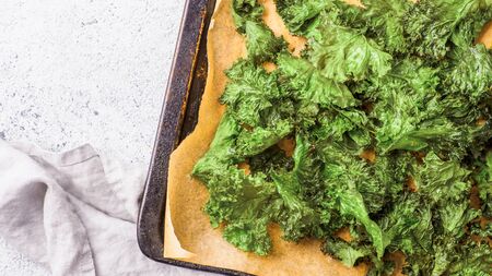Green Kale Chips with salt on oven-tray. Homemade healthy snack for low carb, keto, low calorie diet. Gray cement background. Ready-to-eat kale chips, copy space for text. Bannerの写真素材