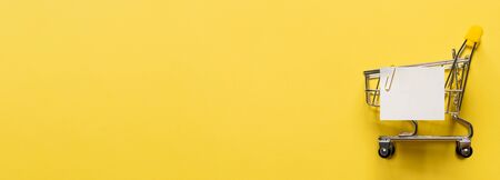 Shopping cart and white paper note list over yellow background. Shopping concept on bright yellow background. Empty white paper note over shopping cart. Copy space for text or design. Bannerの写真素材