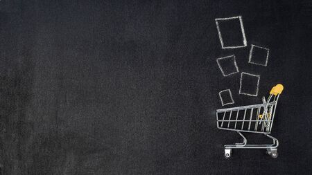 Shopping cart and products on chalkboard. Shop trolley at supermarket as sale, discount, shopaholism concept with copy space left for text or design. Top view or flat lay.の写真素材
