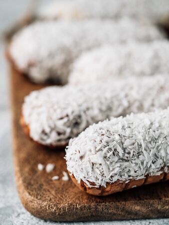 Homemade eclairs with coconut on wooden cutting board. Close up view of delicious healthy profitroles with shredded coconut. Copy space for text or design. Vertical.の写真素材