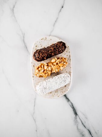 Set of three homemade eclairs on marble background. Top view of delicious healthy profitroles with different decor elements - chocolate, peanut and sherdded coconut. Verticalの写真素材