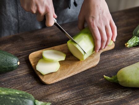Zucchini harvest. Woman slices zucchini on wooden table. Farm organic zucchini harvestingの写真素材