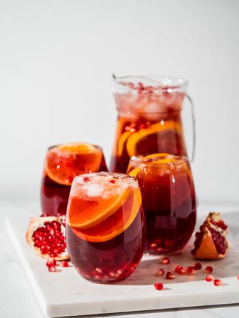 Winter sangria on white marble background. Jugful of sangria and glasses with orange slice and pomegranate. Copy space for text or design. Vertical.の写真素材