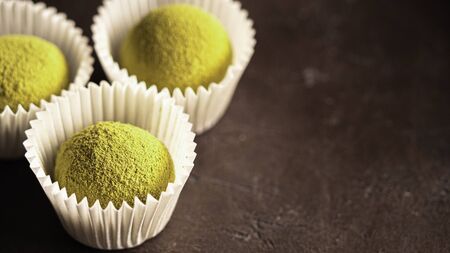 Homemade truffles candy with matcha tea powder in white paper cups on dark background. Copy space right for text or design. Shallow depth of field. Bannerの写真素材