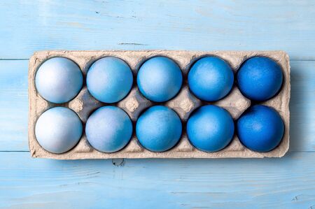 Easter concept. Ombre eggs in blue colors in cardboard packaging on blue wooden background. Top down...