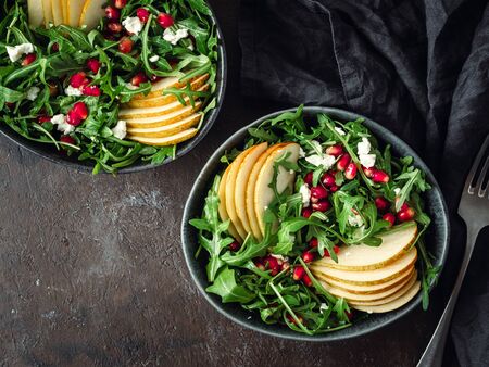 Vegan salad bowl with arugula, pear, pomegranate, coconut crumble or cottage cheese on black background. Vegan breakfast, vegetarian food, diet concept. Top view or flat lay. Copy space for text.の写真素材