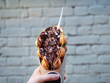 Hong Kong waffles in female hand on brick wall background. Delicious bubble waffle with chocolate...