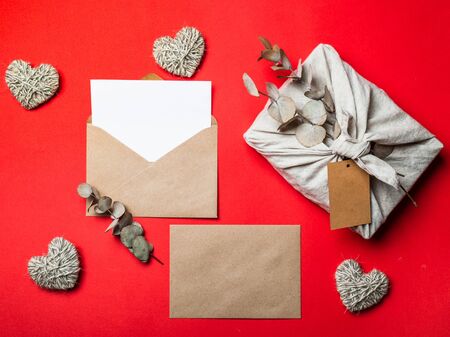 Zero waste Valentine's Day concept and mock up on red. Eco-friendly gift cloth wrapping in Furoshiki style, craft paper envelope,empty greetings card. Top down view or flat lay. Copy space for designの写真素材