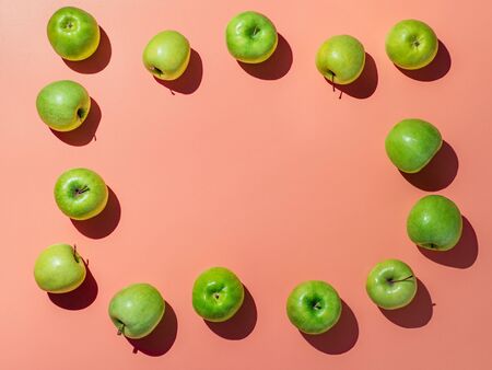 Green apples on orange or coral pink background with copy space for text or design in center, Colorful fruit frame. Flat lay or top view, Hard lightの写真素材