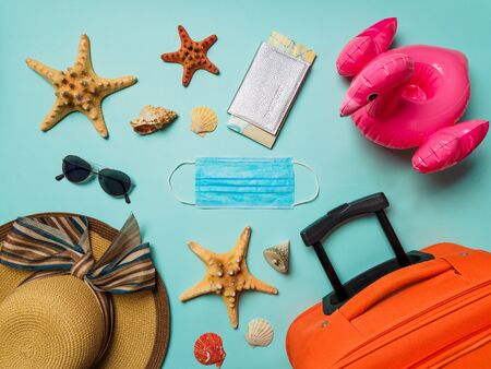 Coronavirus covid-19 and travel concept. Summer vacation and beach rest symbols and breathing mask on blue background. Flat lay or top view.の写真素材