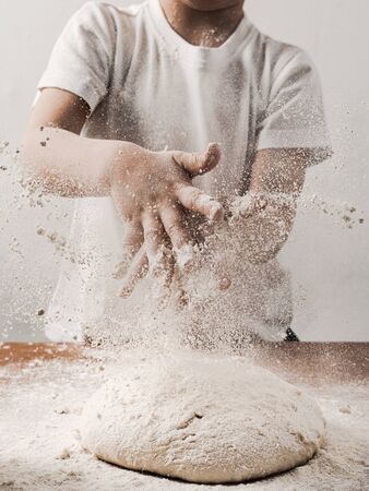 Crop unrecognizable child person clapping hands with flour while cooking bread sprinkling white flour over blob of dough. Vertical. Copy space bottomの写真素材
