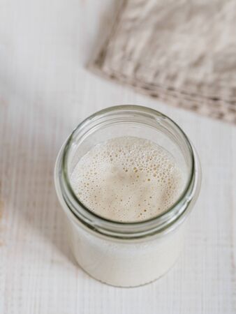 Wheat sourdough starter. Top view of glass jar with sourdough starter on white wooden background. Copy space for text or design. Vertical.の写真素材