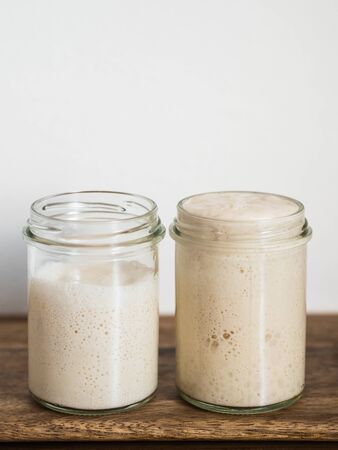 Two glass jars with wheat sourdough starters in different hydration levels. Starter 100 percent...