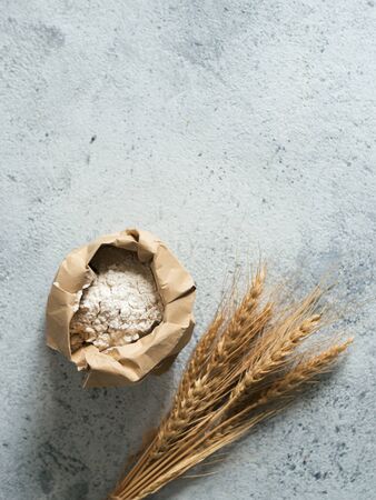 Wheat flour in paper bag and spikes over gray cement background. Food and baking ingredient - all-purpose flour with copy space, verticalの写真素材