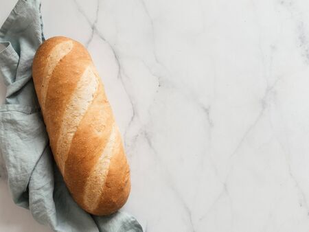 British White Bloomer or European Baton loaf bread on white marble background. Top view or flat lay....